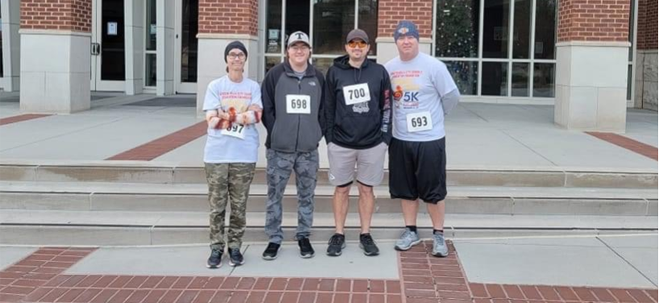 four men standing in row with race numbers on shirts before company 5k starts