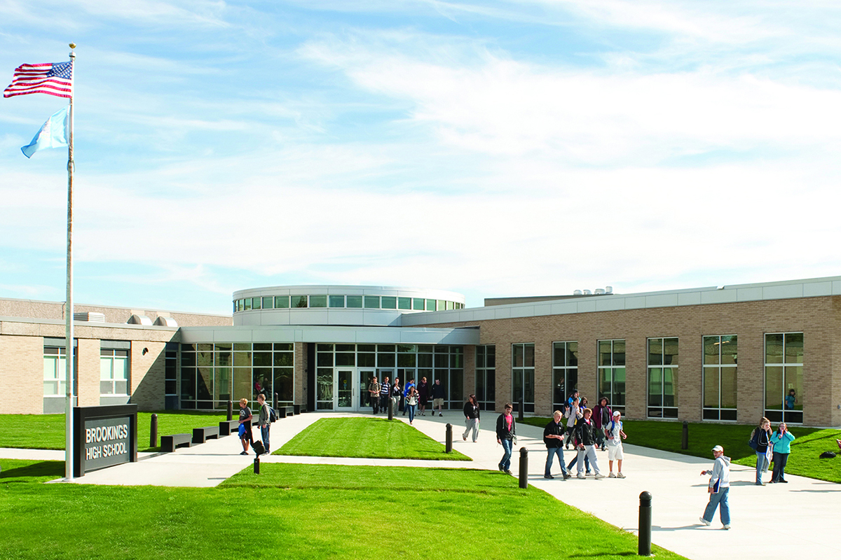 wide outside image of school building with flagpole and students walking