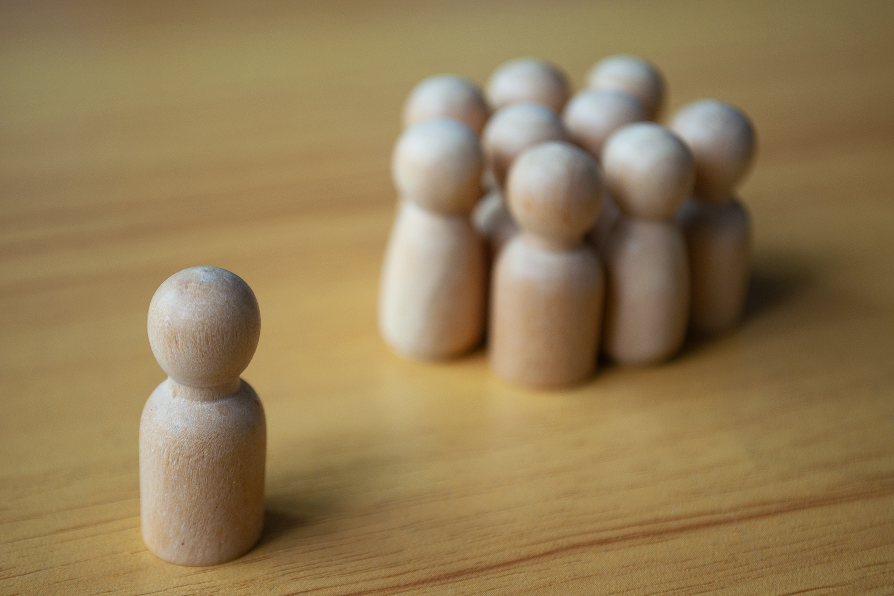 A single wooden doll separated by other dolls representing loneliness and isolation.