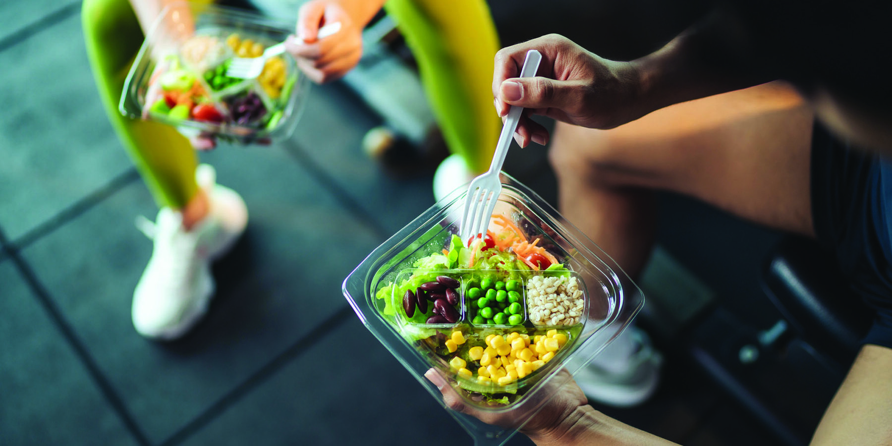 Top view Asian man and woman healthy eating salad after exercise at fitness gym. Two athlete eating salad for health together. Selective focus on salad bowl on hand.