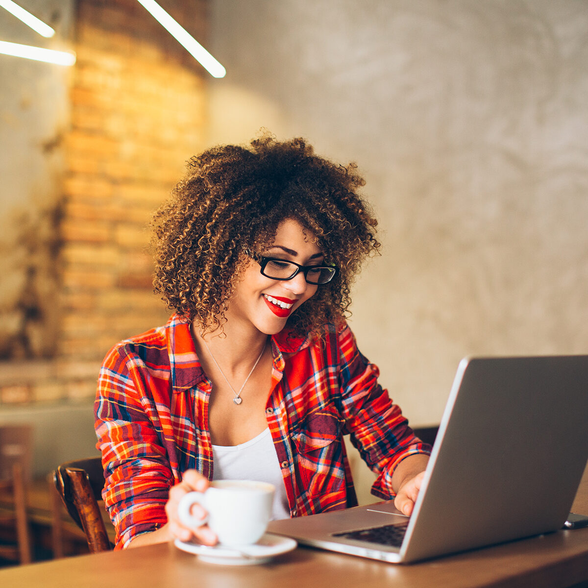 Young woman siting at cafe drinking coffee and working on laptop