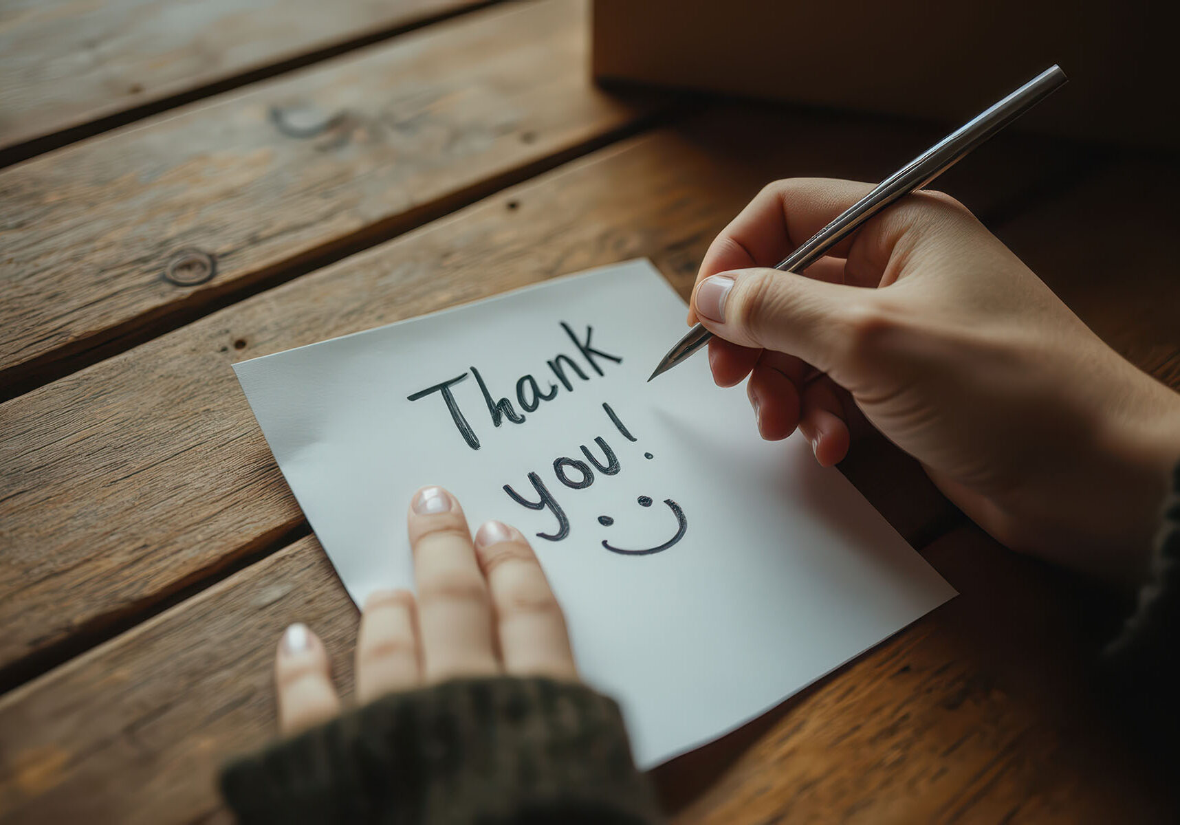 close up of two hands with pen writing 'thank you' on note